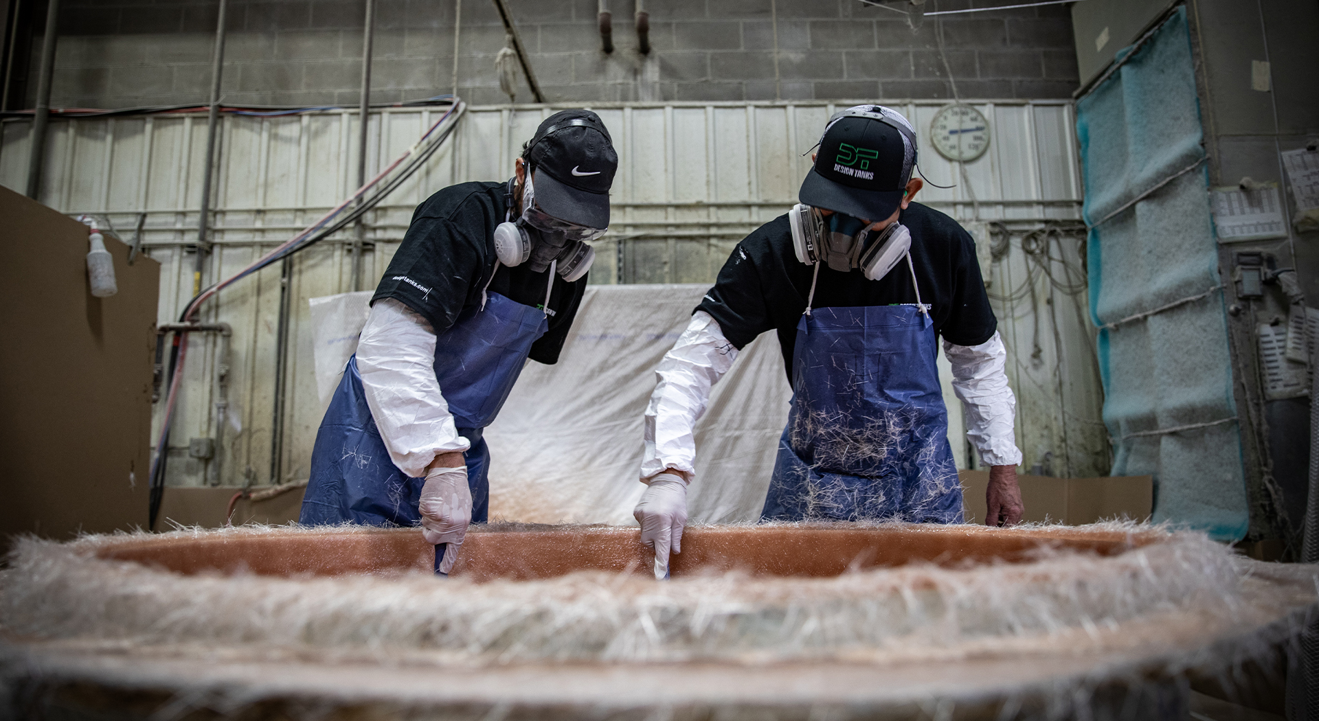 Two men wearing filtration masks building a fiberglass tank.