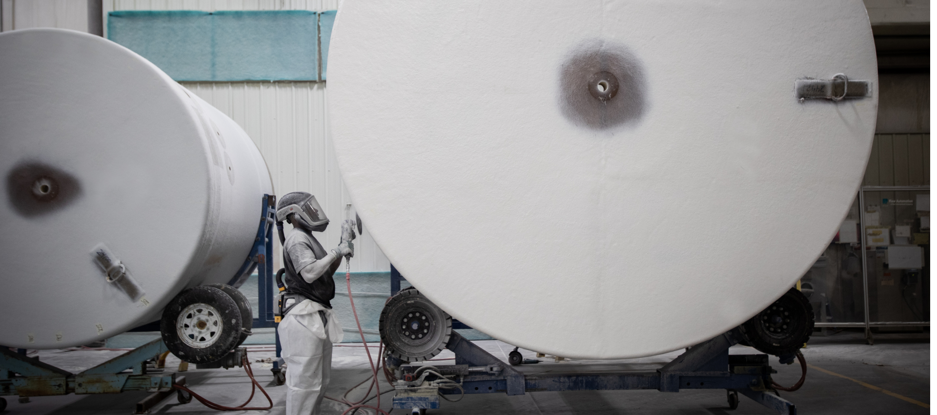 A Design Tanks worker sands the outside of a large fiberglass tank