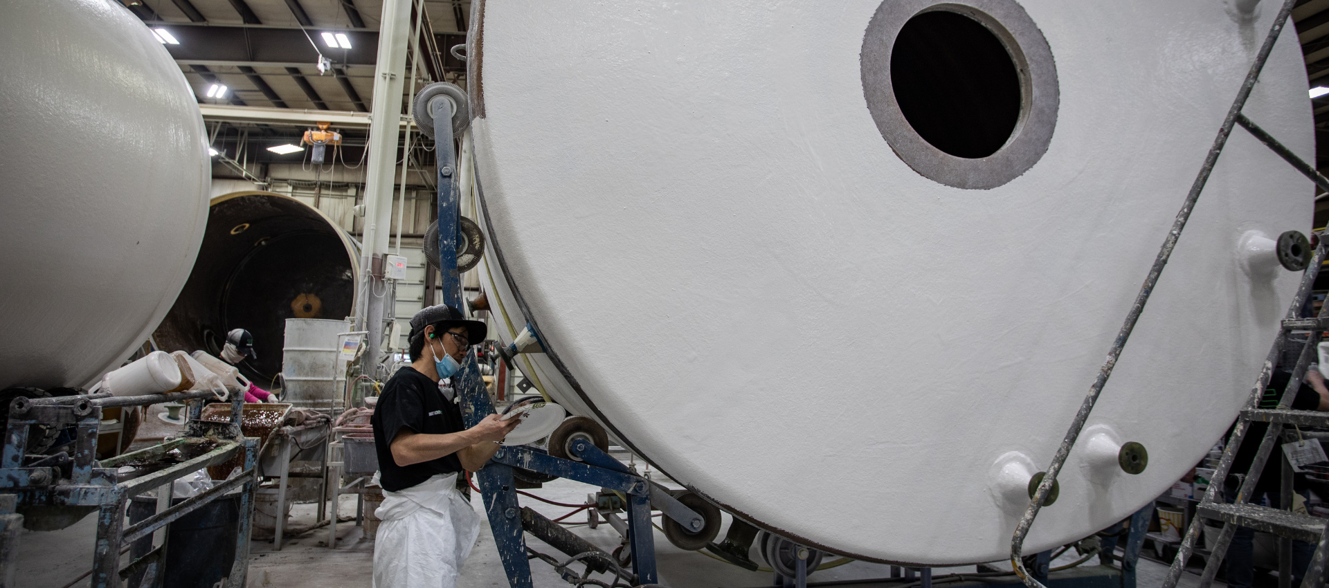 An employee works on sanding a fiberglass tank